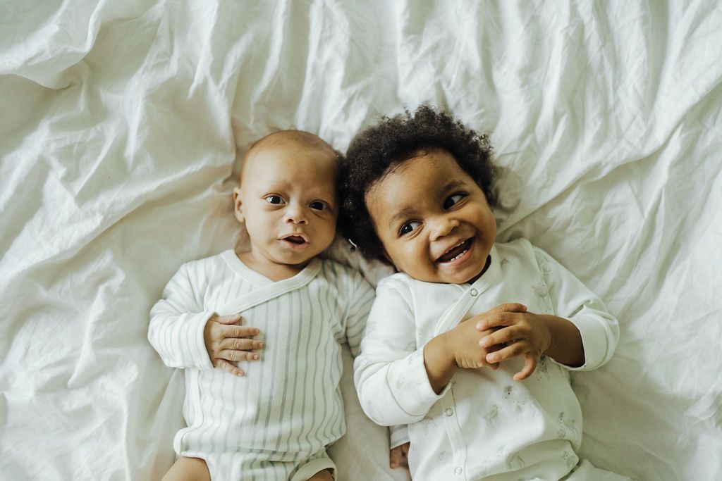 two babies wearing pehr clothing lying on a bed.